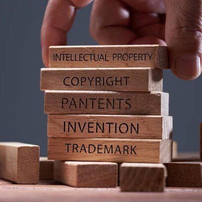 man adding a  block showing the words Intellectual property on top of  other wooden block with text copyright, patents,  invention,and trademark
